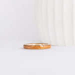 a slim, rounded yellow gold wedding band with a center inlay of american elm wood, giving it a tone on tone look