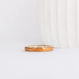 a slim, rounded yellow gold wedding band with a center inlay of american elm wood, giving it a tone on tone look