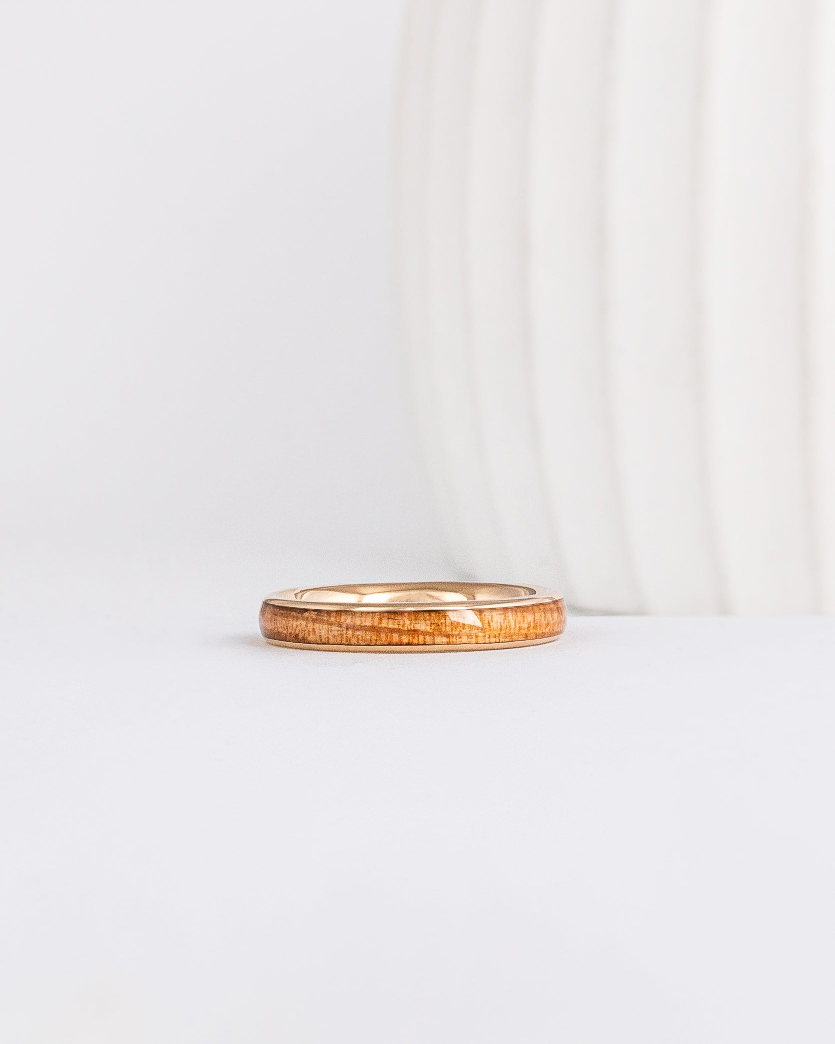 a slim, rounded yellow gold wedding band with a center inlay of american elm wood, giving it a tone on tone look
